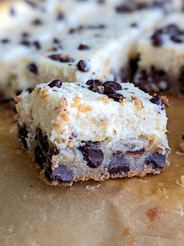 Chocolate chip cookie cheesecake bars, cut into squares and seen close up from the side to show texture.