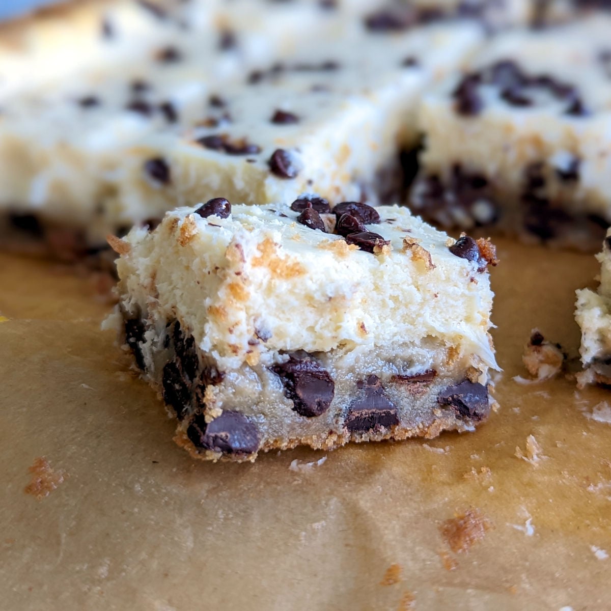 Chocolate chip cookie cheesecake bars, cut into squares and seen close up from the side to show texture.