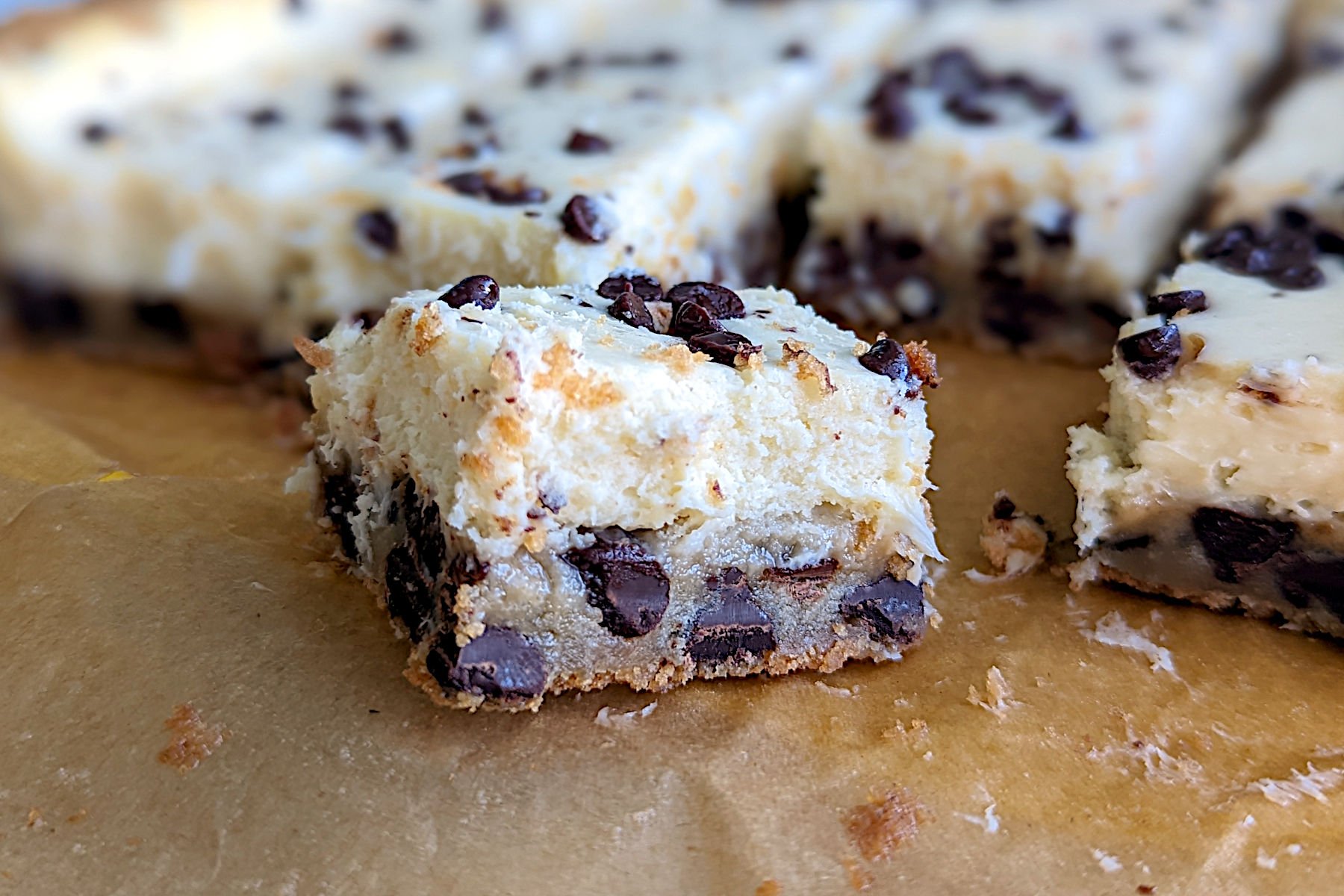Chocolate chip cookie cheesecake bars, cut into squares and seen close up from the side to show texture.