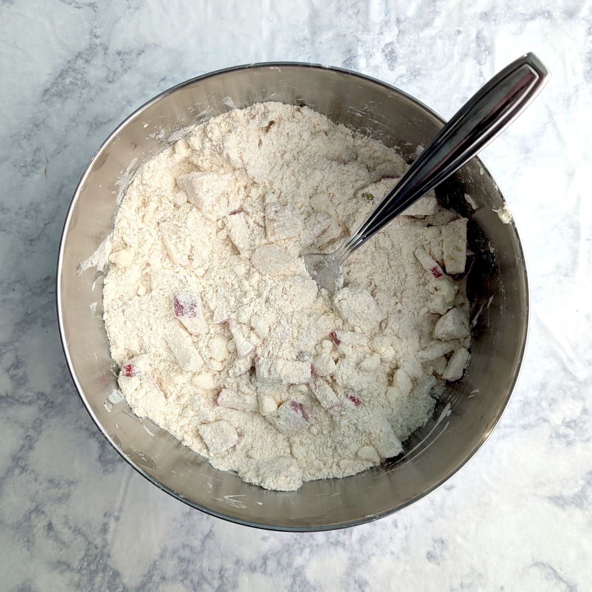 Small pieces of diced apple and pear, tossed in a butter-flour mixture in a mixing bowl.