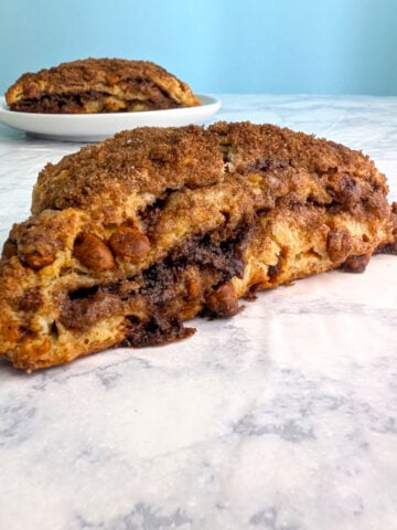 A layered cinnamon scone, seen from the side to see layers. Another scone on a plate is behind it.
