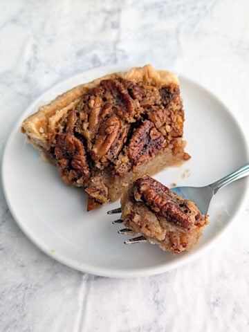 A bite of classic pecan pie on a fork, resting next to the slice of pecan pie on a plate.