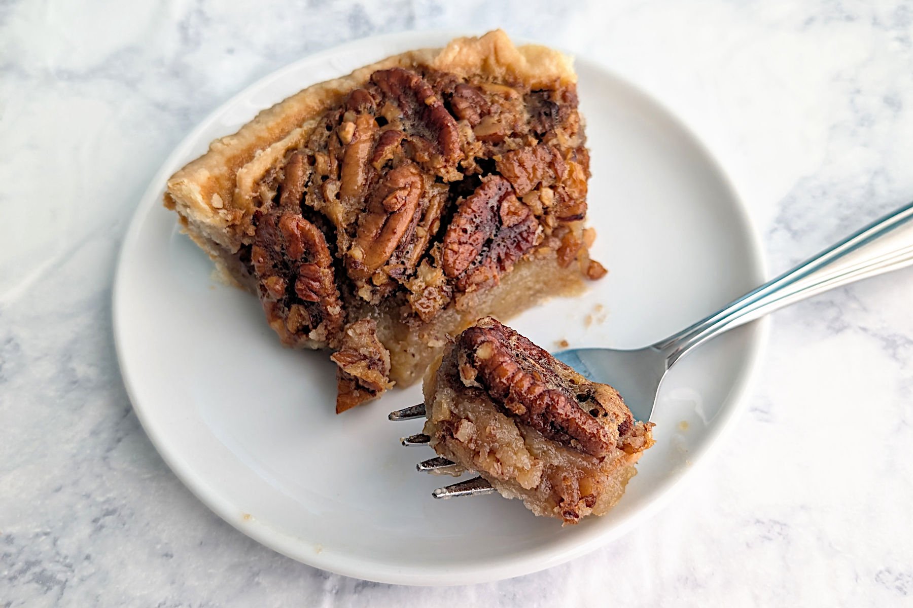 A bite of classic pecan pie on a fork, resting next to the slice of pecan pie on a plate.