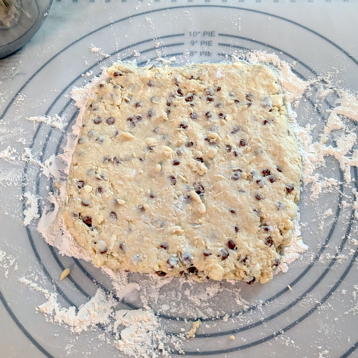 Scone dough with cinnamon chips, patted out into a 9x9 inch square on a reusable baking mat.