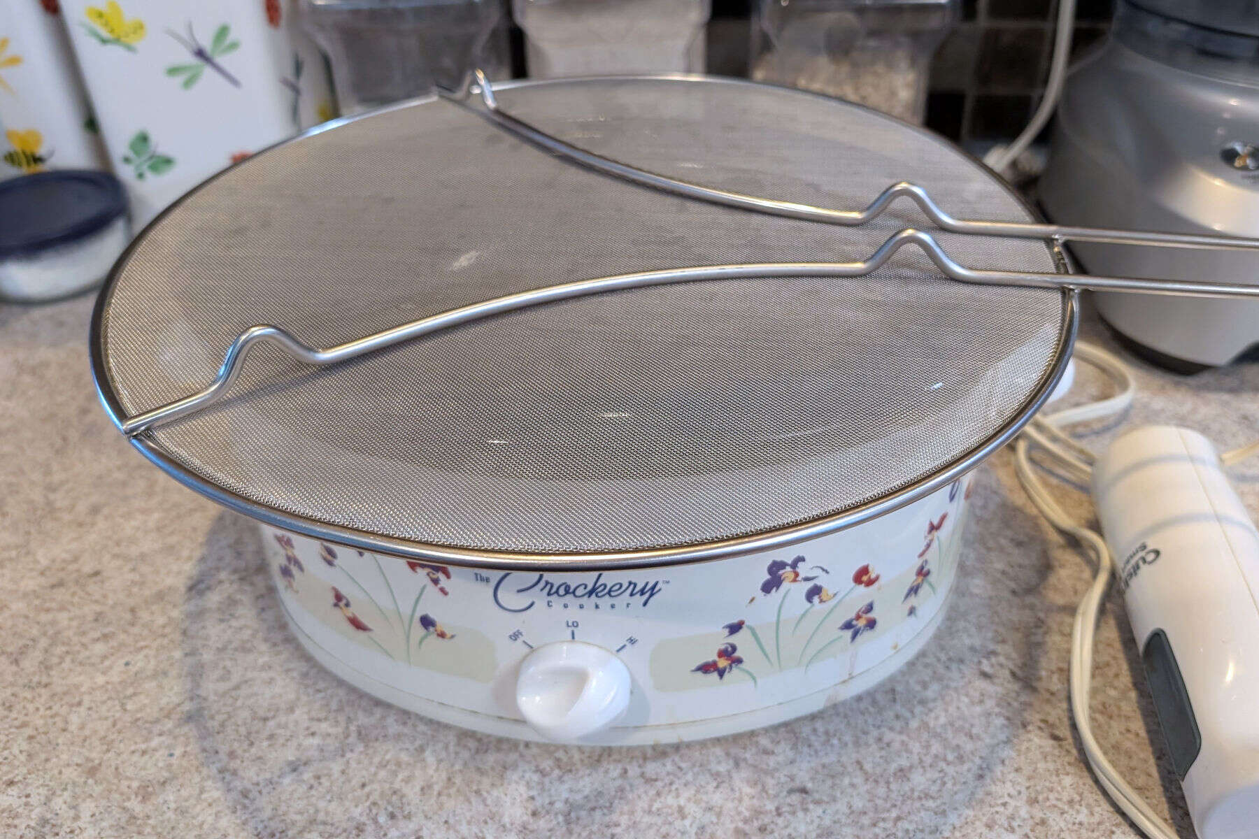 A mesh splatter guard covers a slow cooker in place of a lid.