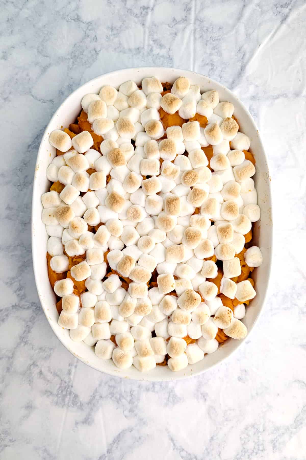 Soft sweet potatoes in a baking dish, with miniature marshmallows baked and browned on top.