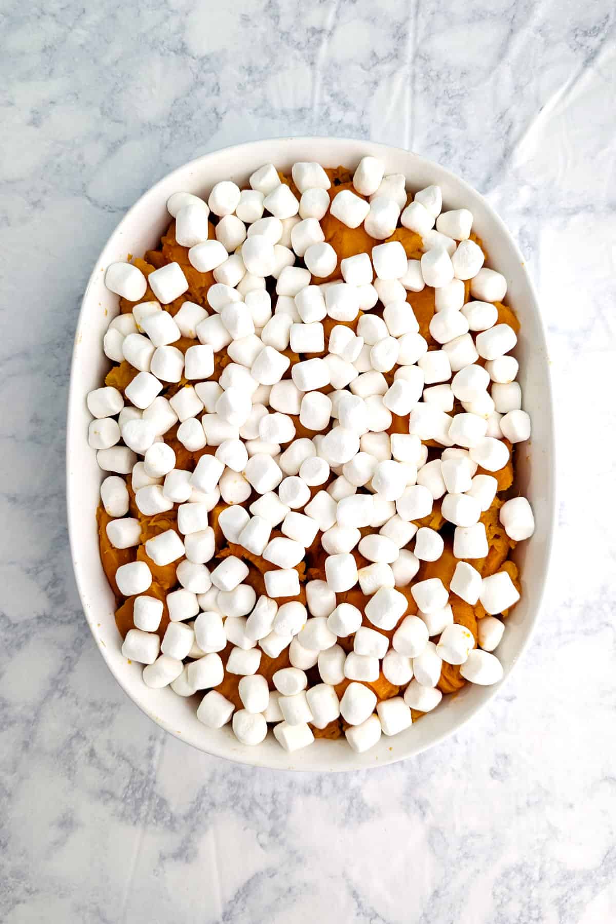 Soft sweet potatoes in a baking dish, topped with miniature marshmallows.