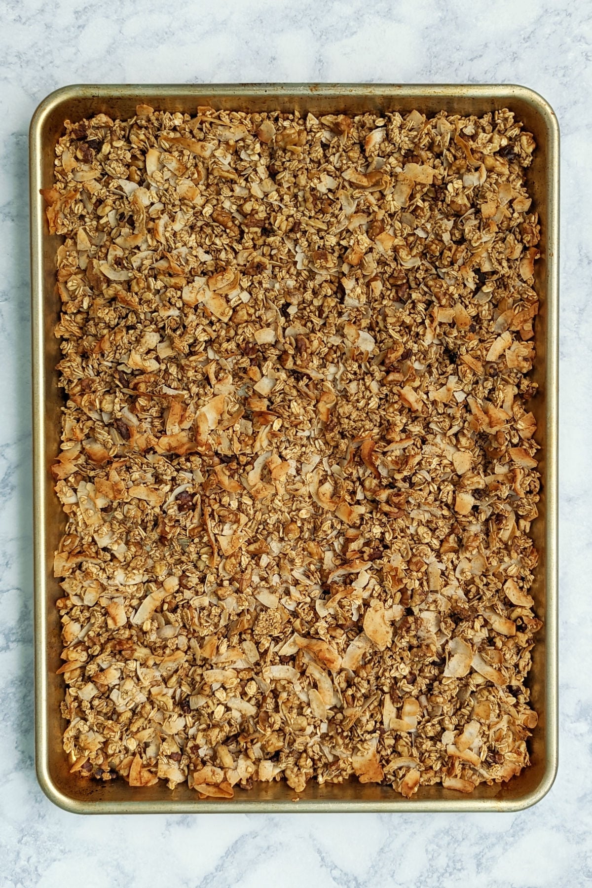 Aquafaba granola with oats, coconut, and walnuts, baked, on a large baking sheet.