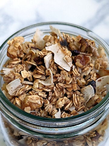 Aquafaba granola with oats, coconut, walnuts, and cinnamon, in a glass jar.