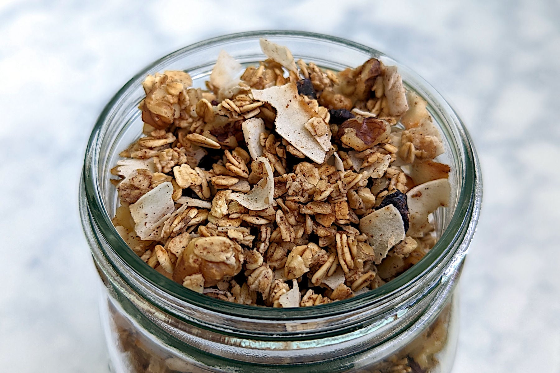 Aquafaba granola with oats, coconut, walnuts, and cinnamon, in a glass jar.