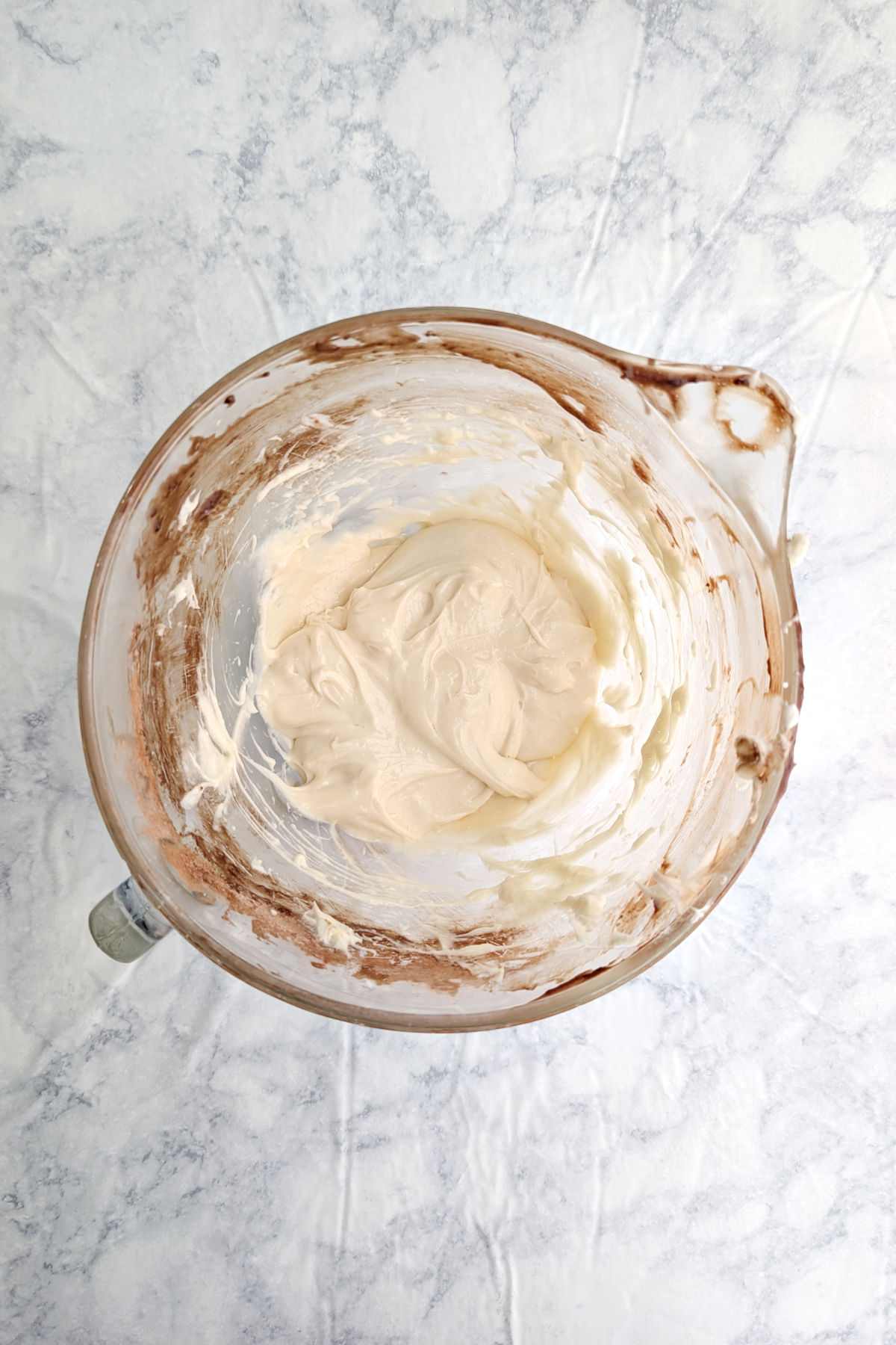 Beaten cream cheese, sugar, and eggs in a glass mixing bowl that still has a small amount of brownie batter residue.