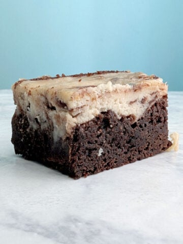 One cheesecake brownie seen from a side angle, to show distinct layers of cheesecake on top of brownie.
