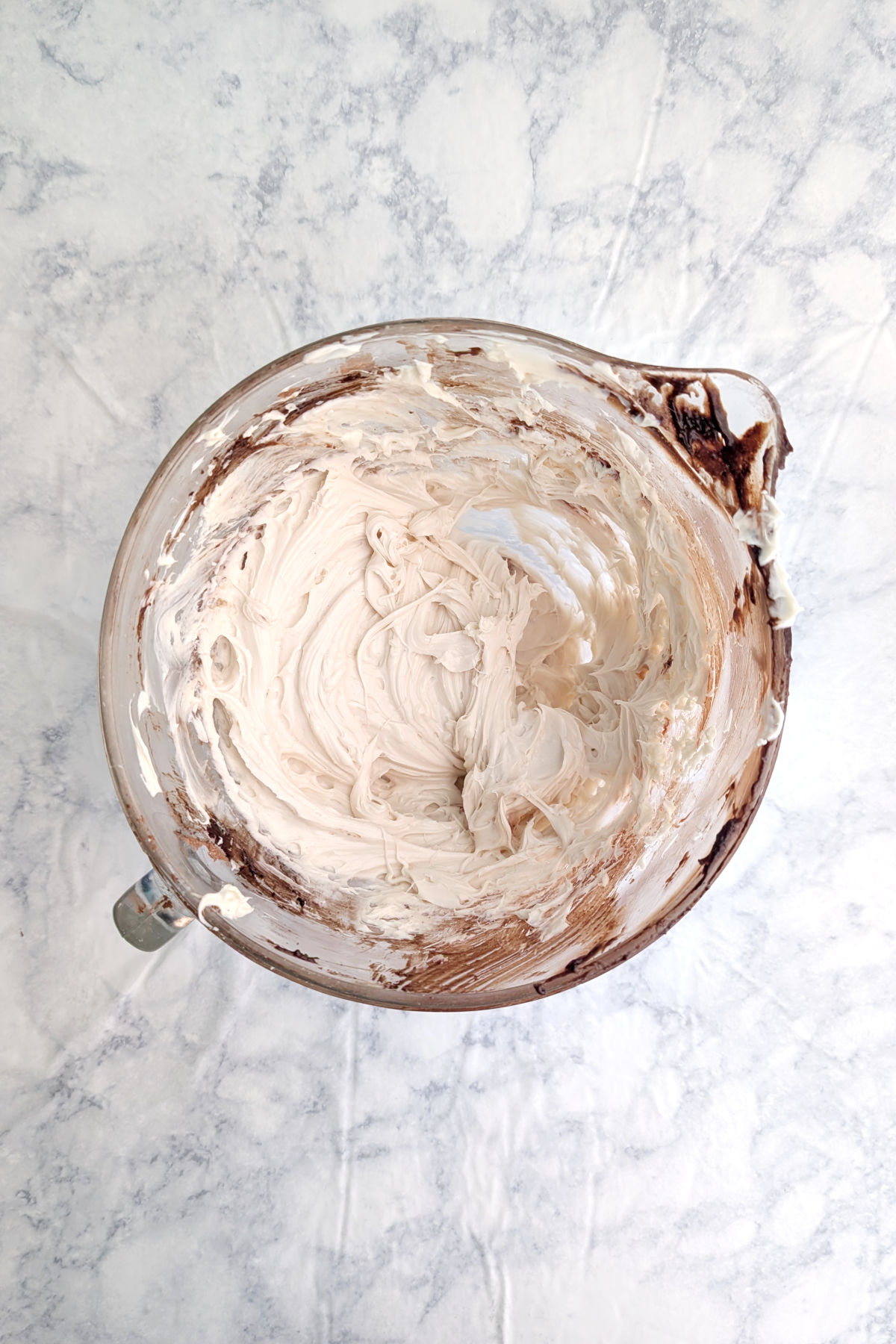 Beaten cream cheese and sugar, in a glass bowl that has a small amount of brownie batter residue in it.