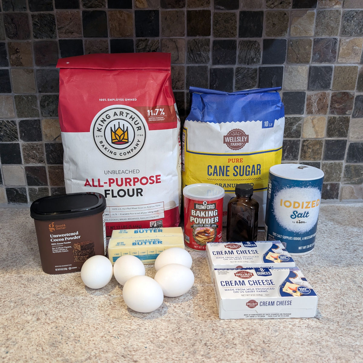 Ingredients for cheesecake brownies: flour, sugar, cocoa powder, butter, eggs, baking powder, vanilla extract, salt, two bricks of cream cheese.