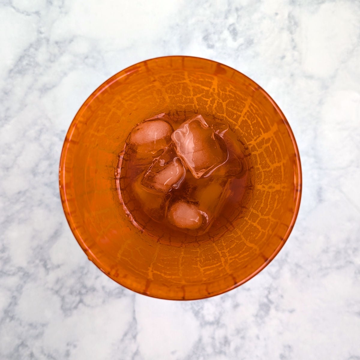 Whiskey, sherry, pecan syrup, lemon juice, and ice, in an orange cocktail shaker seen from directly overhead.