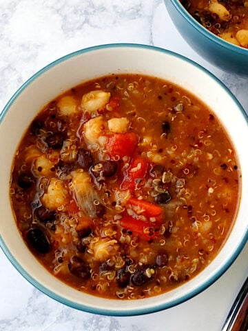 A bowl of Mexican soup on a table next to a spoon, with another bowl nearby.
