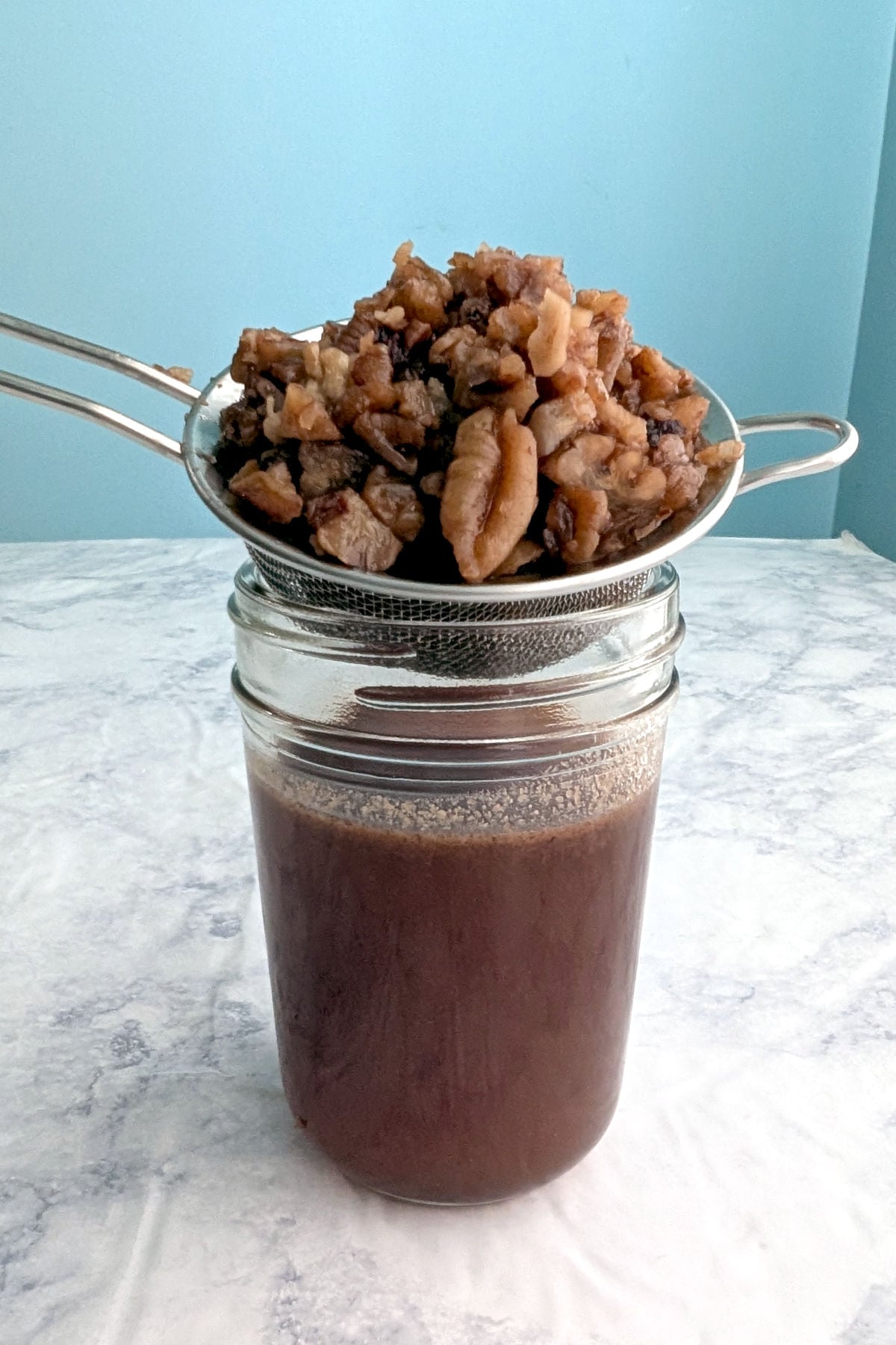 A strainer holding pecans rests on a small glass jar that holds toasted pecan syrup.