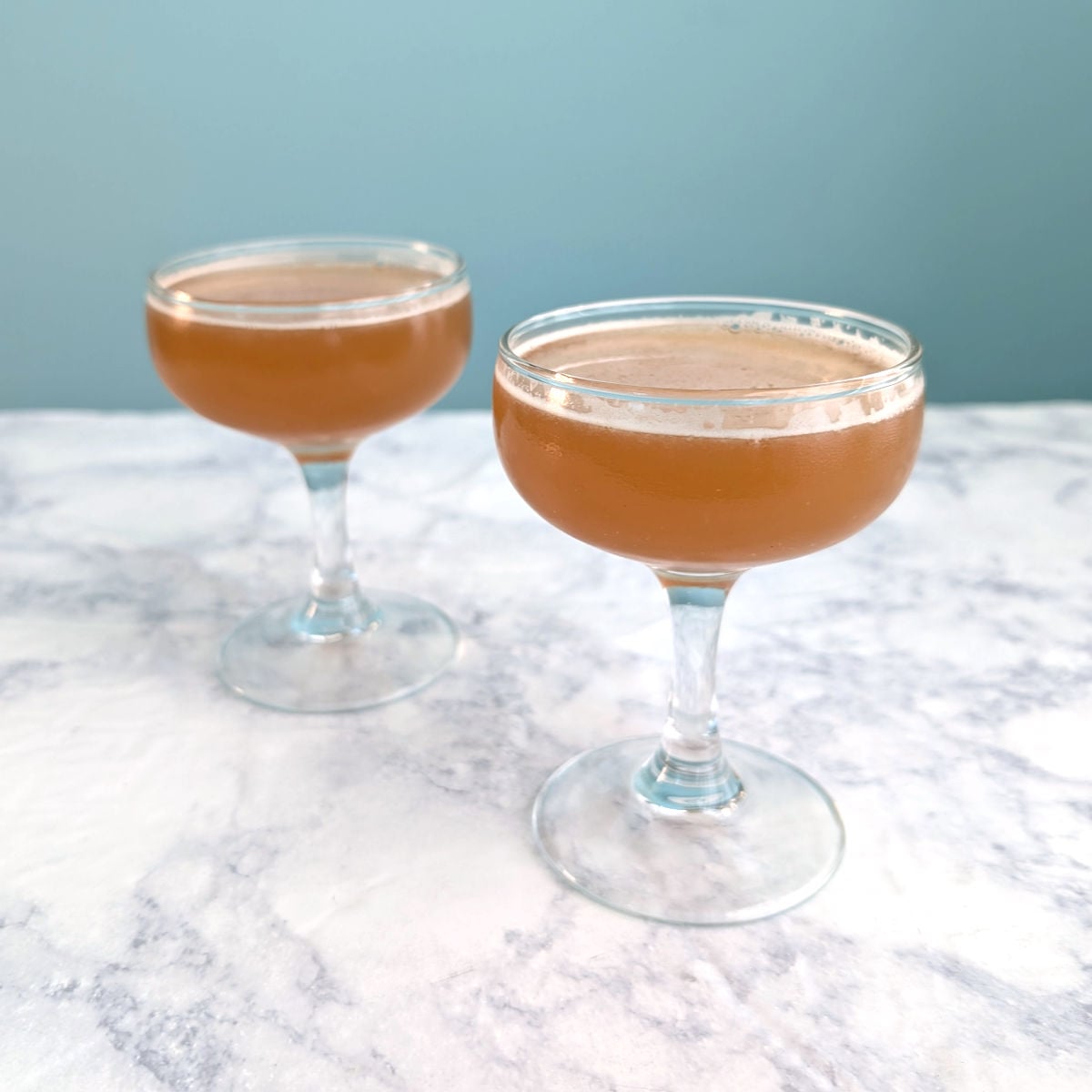 Two coupe glasses with whiskey-sherry cocktail.