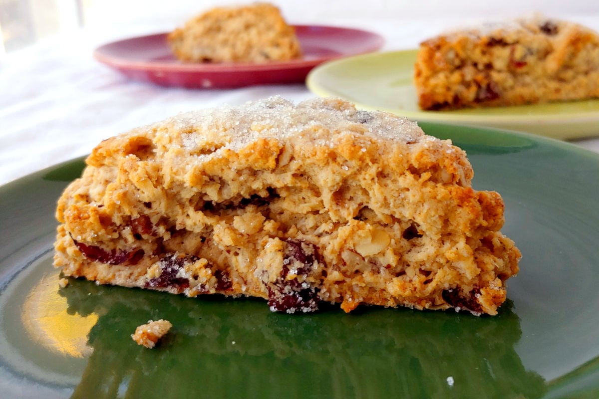 A Cranberry Oat Pecan Scone on a green plate. Other scones are on red and green plates in the background.