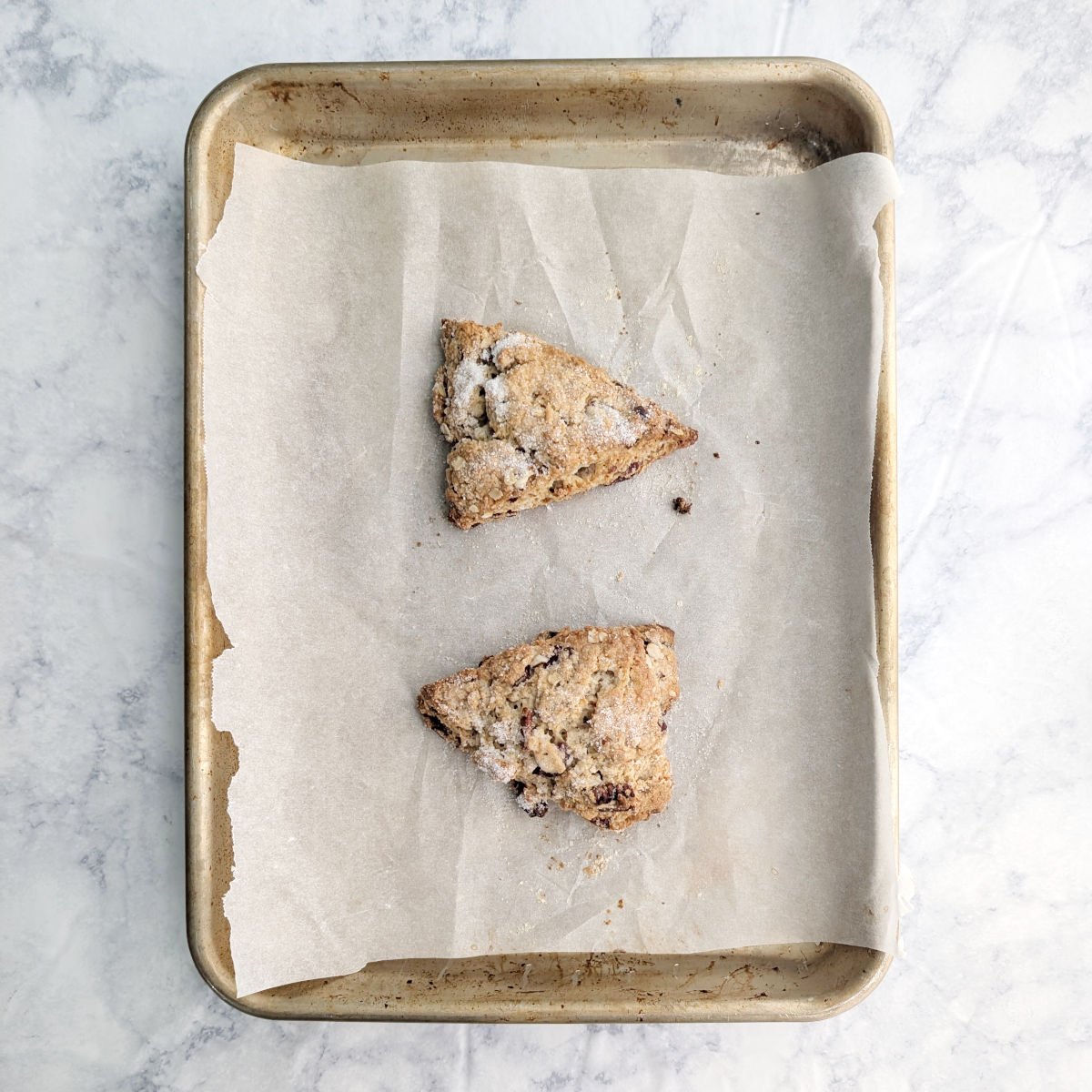 Two baked cranberry oat pecan scones, on a small parchment lined baking sheet.