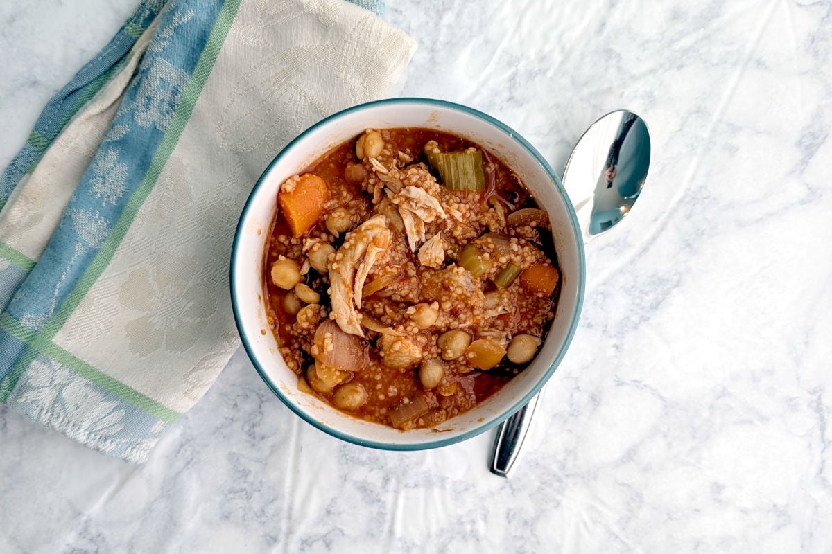 A bowl of Stewed Chicken and Chickpeas, with a spoon and a napkin.