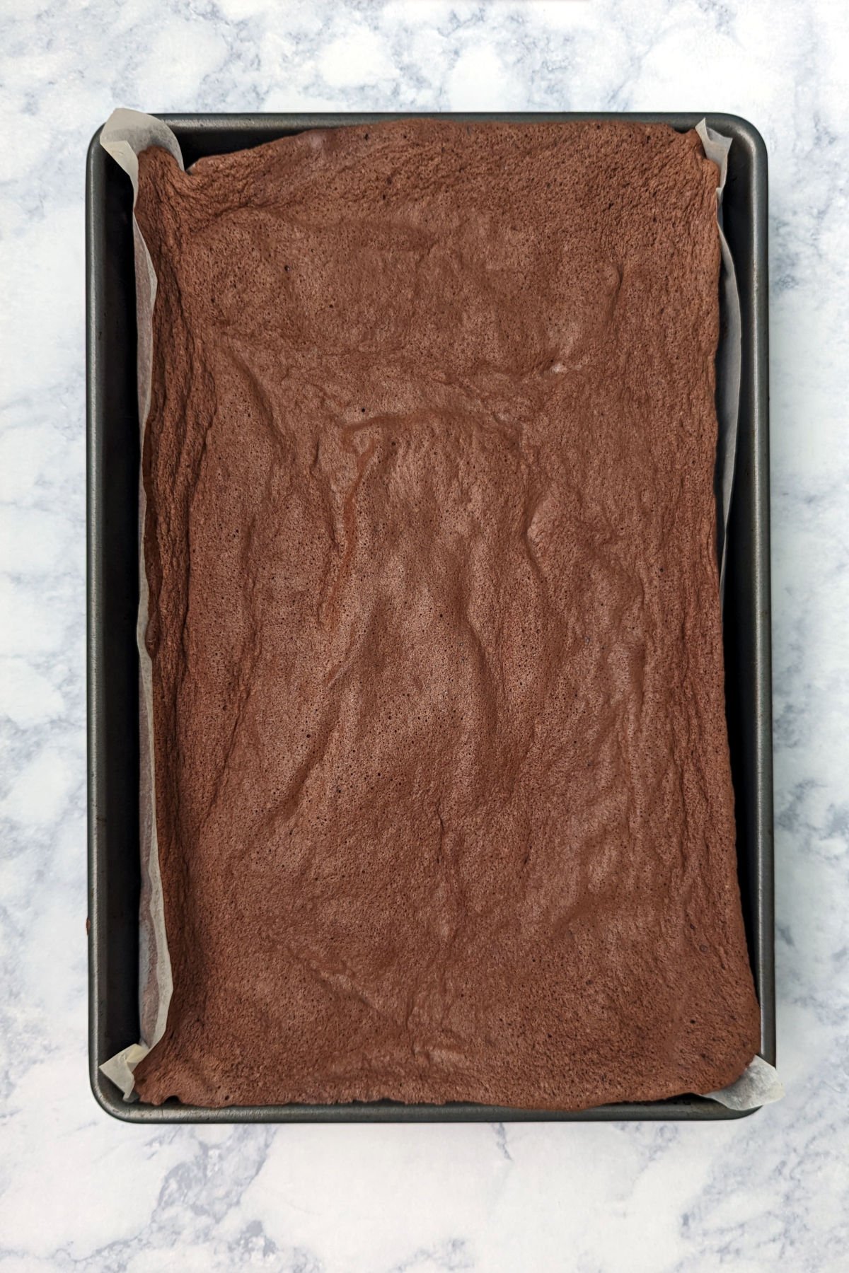 Flourless chocolate sponge cake, baked, in a jelly roll pan lined with parchment paper.