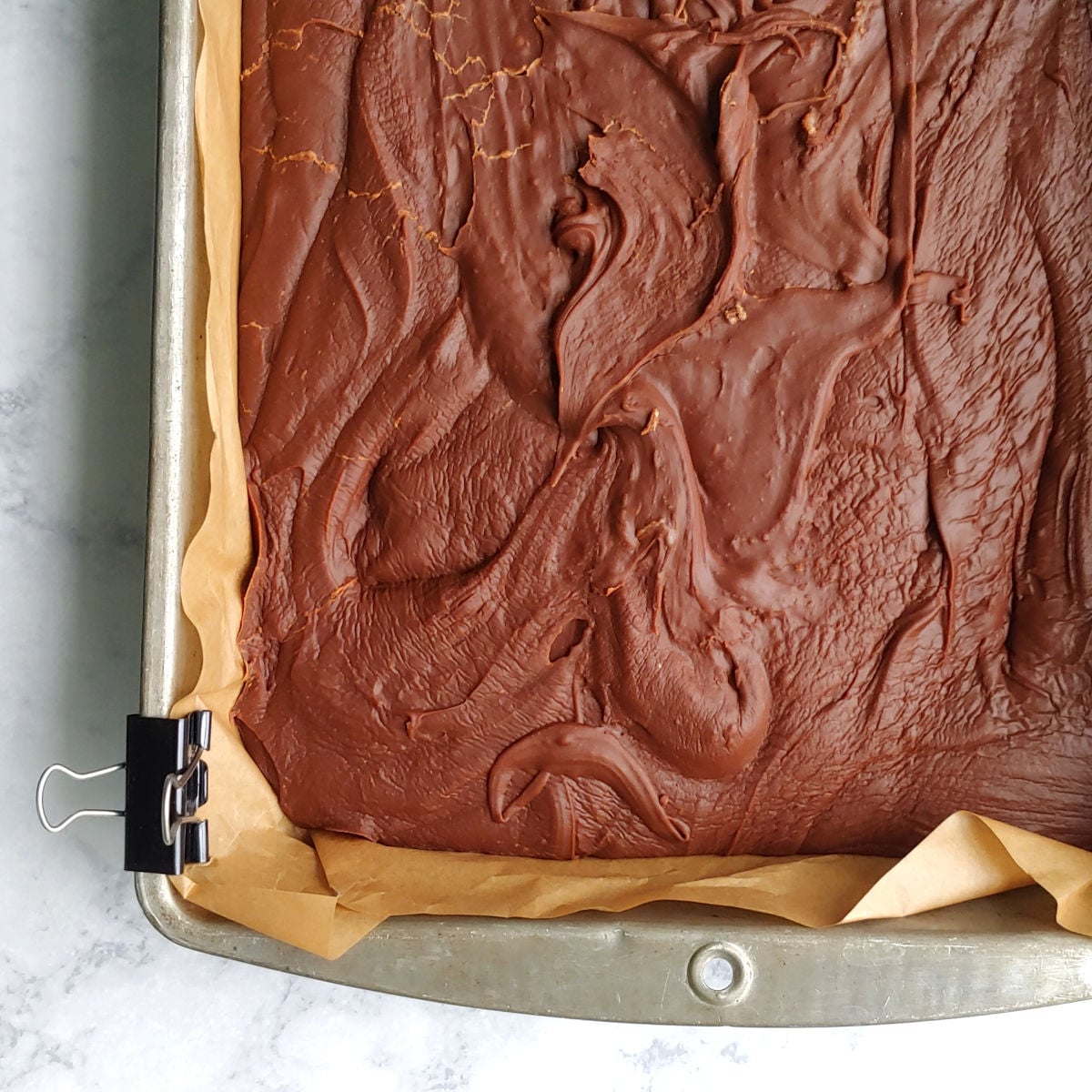 Cooled and set homemade chocolate fudge in a parchment-lined pan, seen up close.