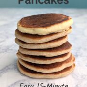 A stack of seven pancakes on a table. The top one is made with all-purpose flour; the bottom six are made with half all-purpose and half whole wheat flour. Text overlay reads "Fluffy Homemade Pancakes. Easy 15-minute One-Bowl Recipe. Easy As Cookies."