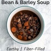 A bowl of slow cooker southwestern bean and barley soup, with beans and carrots visible on the top. Text overlay reads, "Slow Cooker Southwestern Bean and Barley Soup. Earthy, Fiber-Filled, Naturally Vegan. Easy As Cookies."