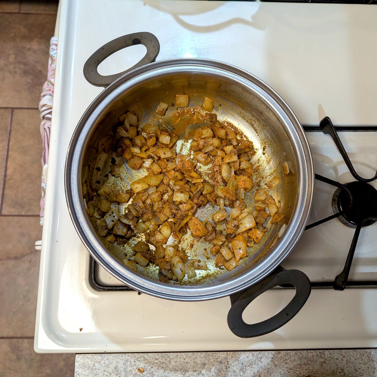 Sauteed onion with turmeric, cumin, and mustard seeds, in a large pot on a stove.