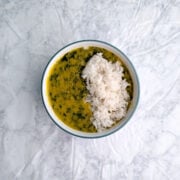 A bowl of lemony lentil soup with spinach and cilantro in a bowl, with a layer of white rice garnishing one side.