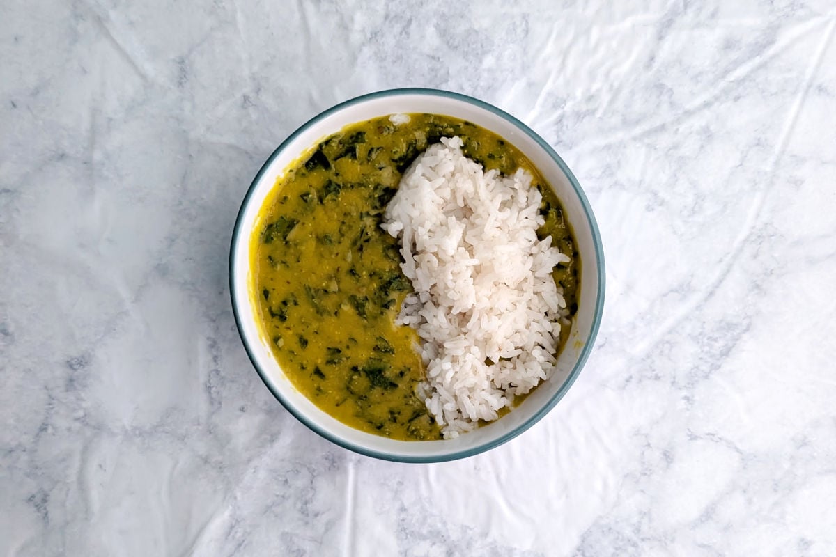 A bowl of lemony lentil soup with spinach and cilantro in a bowl, with a layer of white rice garnishing one side.