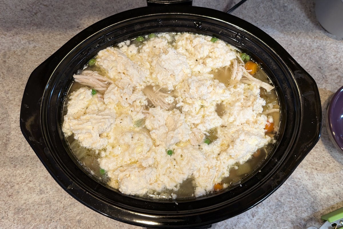 Uncooked dumpling dough on top of chicken soup in a slow cooker.