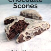 Glazed double chocolate scones on a table. One scone is broken open to show texture. Text overlay reads "Double Chocolate Scones. Rich chocolatey tender. Easy As Cookies."