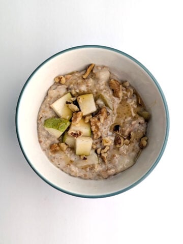 Creamy steel-cut oats with walnuts and pear, in a bowl. The oats are garnished with additional chopped walnuts, pear, and honey.