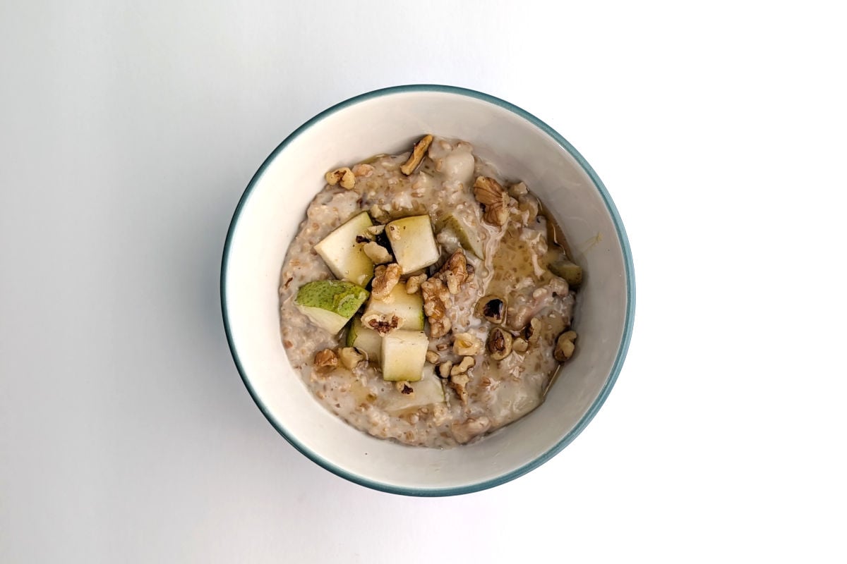 Creamy steel-cut oats with walnuts and pear, in a bowl. The oats are garnished with additional chopped walnuts, pear, and honey.