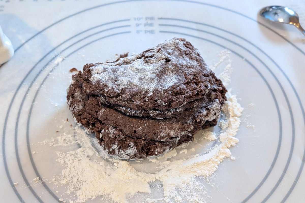 Chocolate scone dough on a floured surface, folded over itself during the process of kneading.