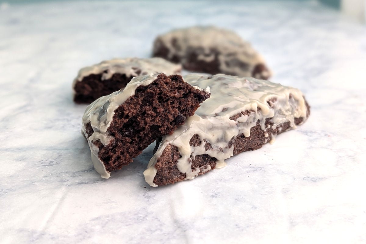 Glazed double chocolate scones on a table. One scone is broken open to show texture.
