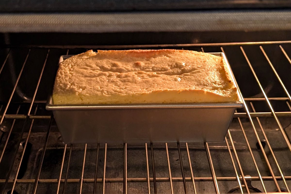 Ricotta pound cake in an 8.5-inch loaf pan, 25 minutes into baking. The cake batter rises above the rim of the pan, but does not spill over.