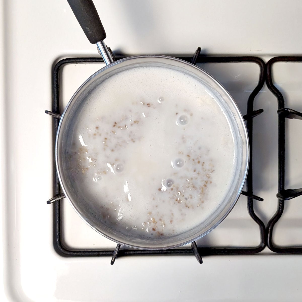 Steel cut oats and milk simmer in a small pot on the stove.