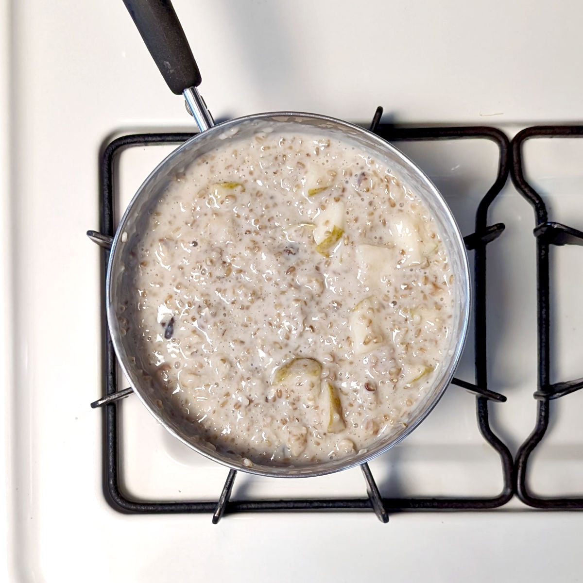 A pot of steel cut oats with walnuts after chopped pears are stirred in, on the stovetop.