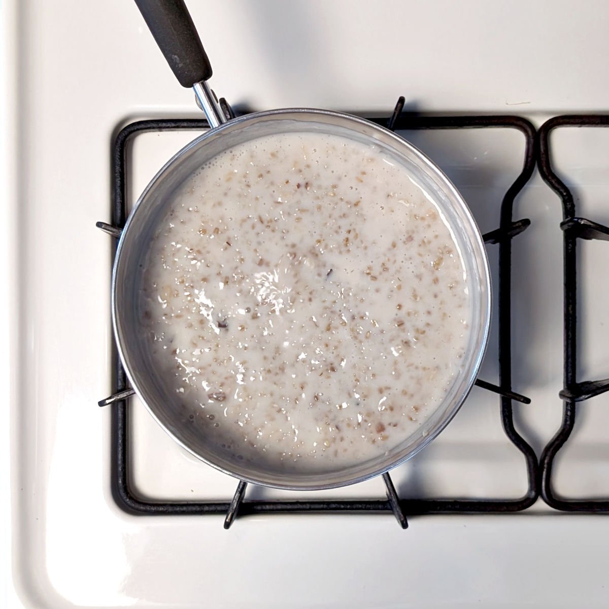 Steel cut oats on the surface of the cooking liquid after stirring in walnuts, in a pot on the stove.