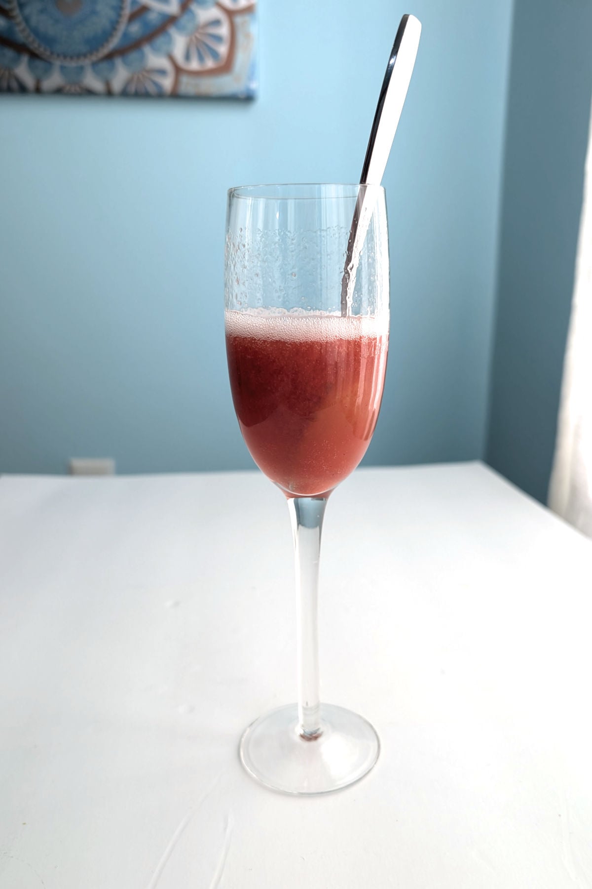 Strawberry bellini puree and prosecco stirred together, in a champagne flute with a spoon.