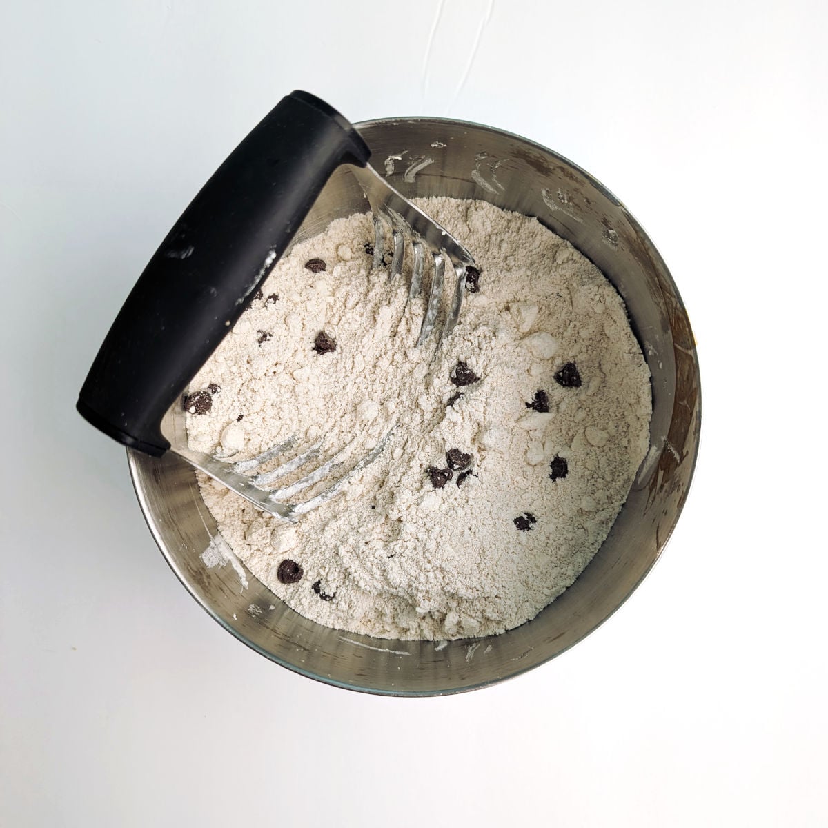 Dry ingredients for chocolate chip cookie scones, with butter cut in and chocolate chips stirred in. A pastry cutter rests in the bowl.
