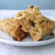 Two chocolate chip cookie scones topped with brown sugar, on a plate. One is torn open to show texture.