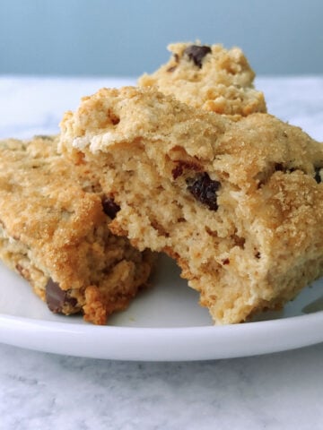 Two chocolate chip cookie scones topped with brown sugar, on a plate. One is torn open to show texture.