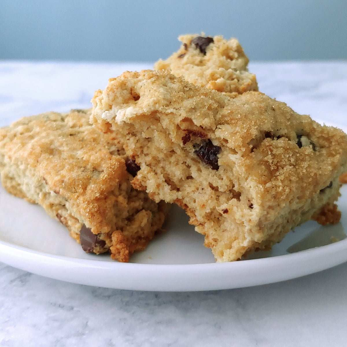 Two chocolate chip cookie scones topped with brown sugar, on a plate. One is torn open to show texture.