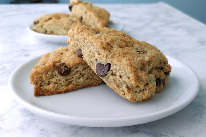 Two chocolate chip cookie scones topped with brown sugar, stacked on a plate.
