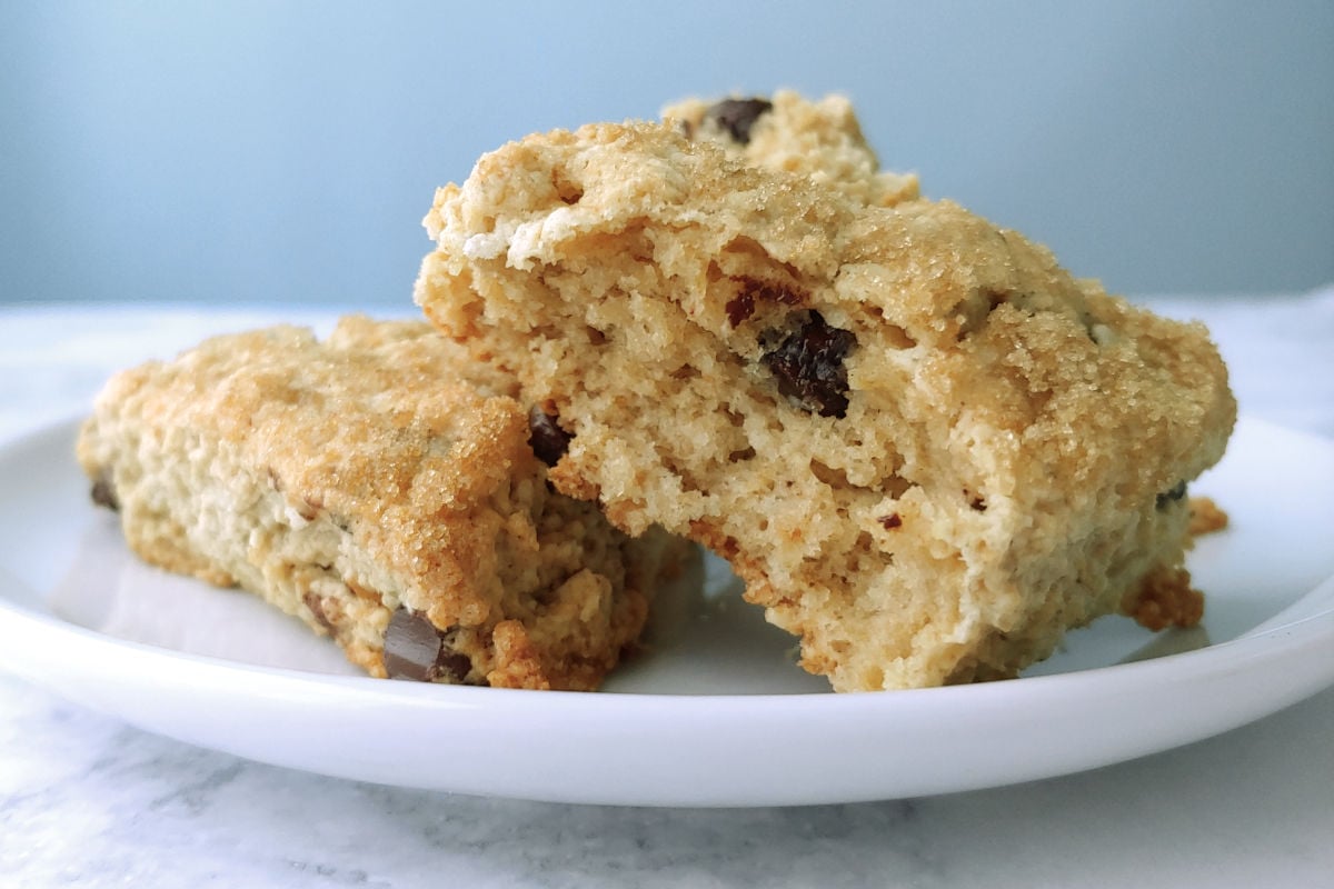Two chocolate chip cookie scones topped with brown sugar, on a plate. One is torn open to show texture.