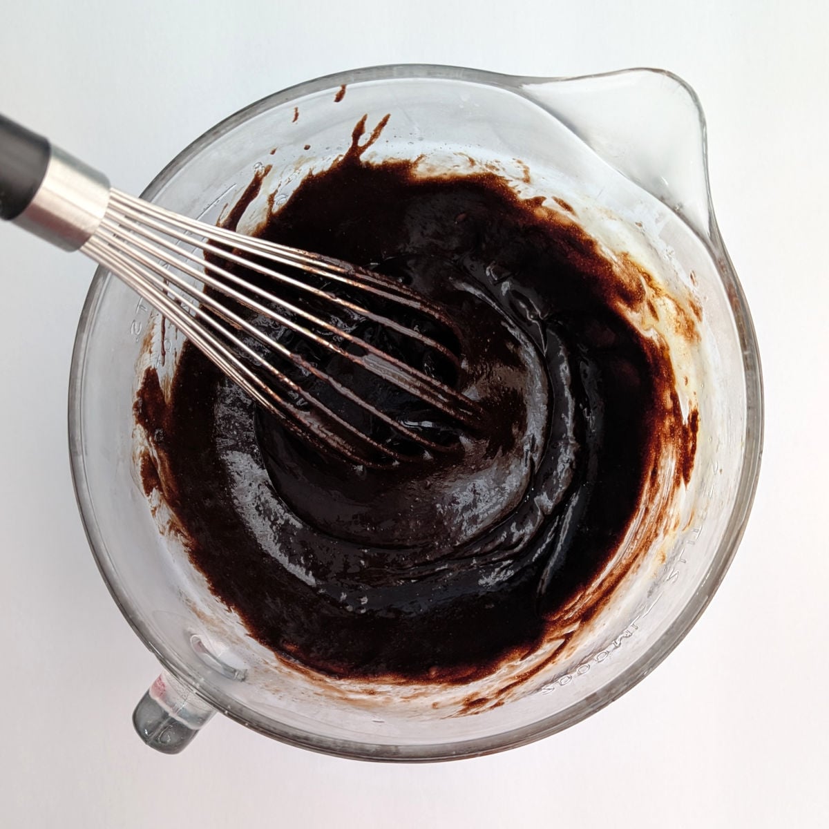 Sugar, melted butter, vanilla, cocoa powder, and eggs, mixed together in a glass 8-cup measuring cup.